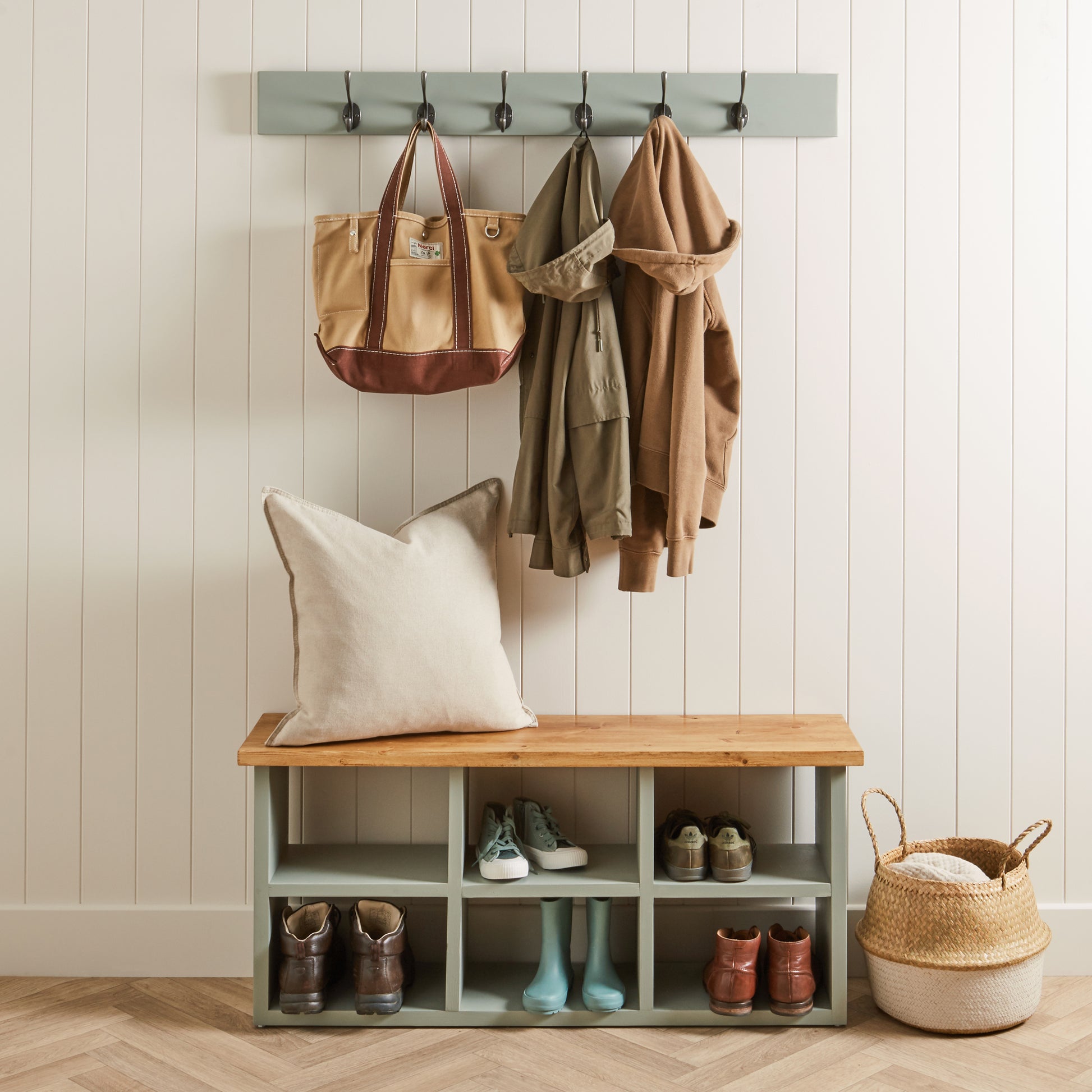 Entryway with wooden bench, coat rack, and storage shelves against a white paneled wall.