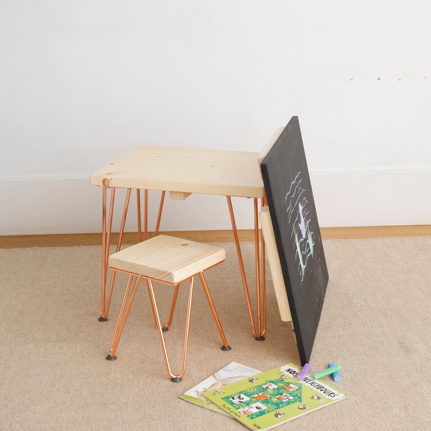 Small wooden table with a chair and children's books on a beige carpeted floor.
