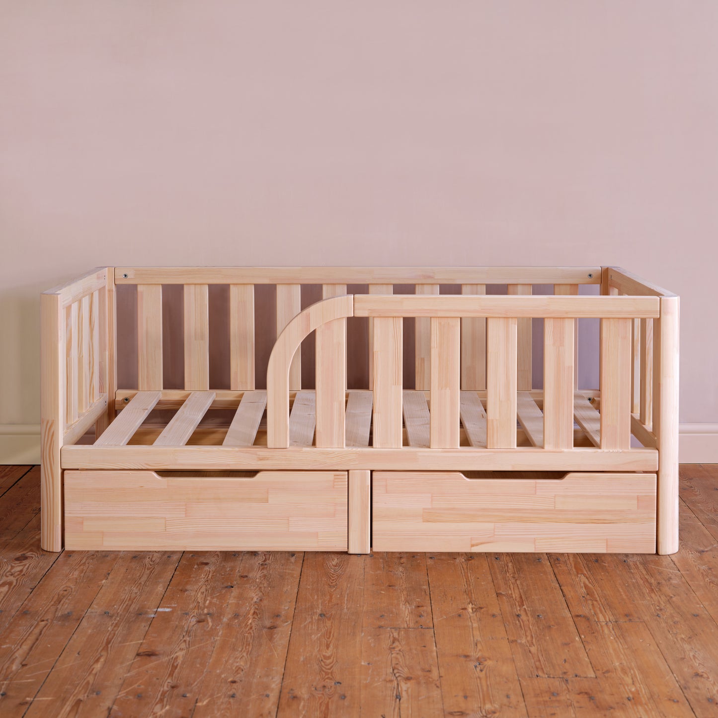 Wooden crib with drawers on a wooden floor against a plain wall