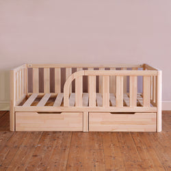 Wooden crib with drawers on a wooden floor against a plain wall