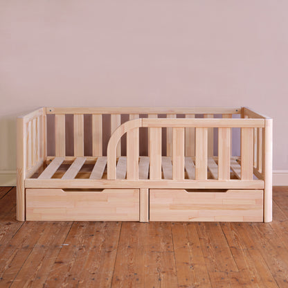 Wooden crib with drawers on a wooden floor against a plain wall