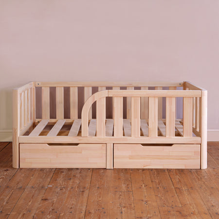 Wooden crib with drawers on a wooden floor against a plain wall